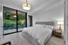 Floor-to-ceiling glass sliding doors opening to an exterior balcony, light-toned wood-finish flooring, and a circular drum pendant light fixture