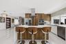 Modern kitchen featuring full-height wood-finish cabinetry, a waterfall-edge center island, quartz countertops, stainless steel appliances, and polish
