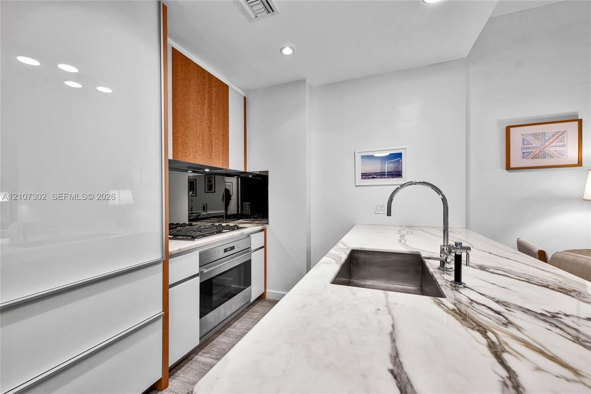 Contemporary kitchen featuring white high-gloss cabinetry, stone-surface countertops, an undermount sink with a gooseneck faucet, stainless steel wall