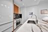 Contemporary kitchen featuring white high-gloss cabinetry, stone-surface countertops, an undermount sink with a gooseneck faucet, stainless steel wall