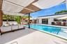 Outdoor living space featuring a covered pergola with textile shade sails, an in-ground swimming pool with integrated step entry, a concrete pool deck