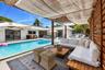 Outdoor patio area featuring a slatted wood privacy wall and an overhead woven fabric canopy, including a rectangular swimming pool surrounded by a co