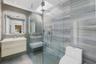 Floating wood-finish vanity with a rectangular sink, walk-in glass-enclosed shower featuring stone-finish wall tile, built-in stone-finish shower benc