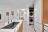 Kitchen island with stone countertop, stainless steel undermount sink, high-arc faucet, wood-finish cabinetry, and built-in laundry closet with stacke