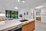Kitchen island with stone countertop, undermount sink, gooseneck faucet, light wood-finish cabinetry, and wood-finish tile flooring