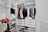Walk-in closet featuring white built-in shelving, multiple hanging rods, and six integrated soft-close drawers with metallic pulls