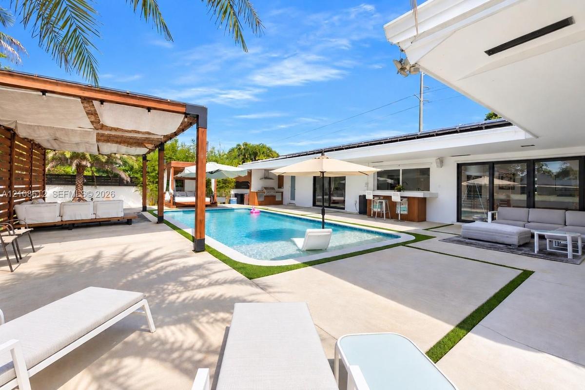 Swimming pool with tanning ledge, expansive concrete patio, built-in outdoor bar, and wood-framed pergola