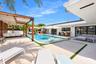 Swimming pool with tanning ledge, expansive concrete patio, built-in outdoor bar, and wood-framed pergola
