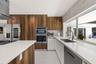 Modern kitchen featuring wood-finish cabinetry, crisp white countertops, high-gloss tile flooring, stainless steel built-in double ovens, and a large 