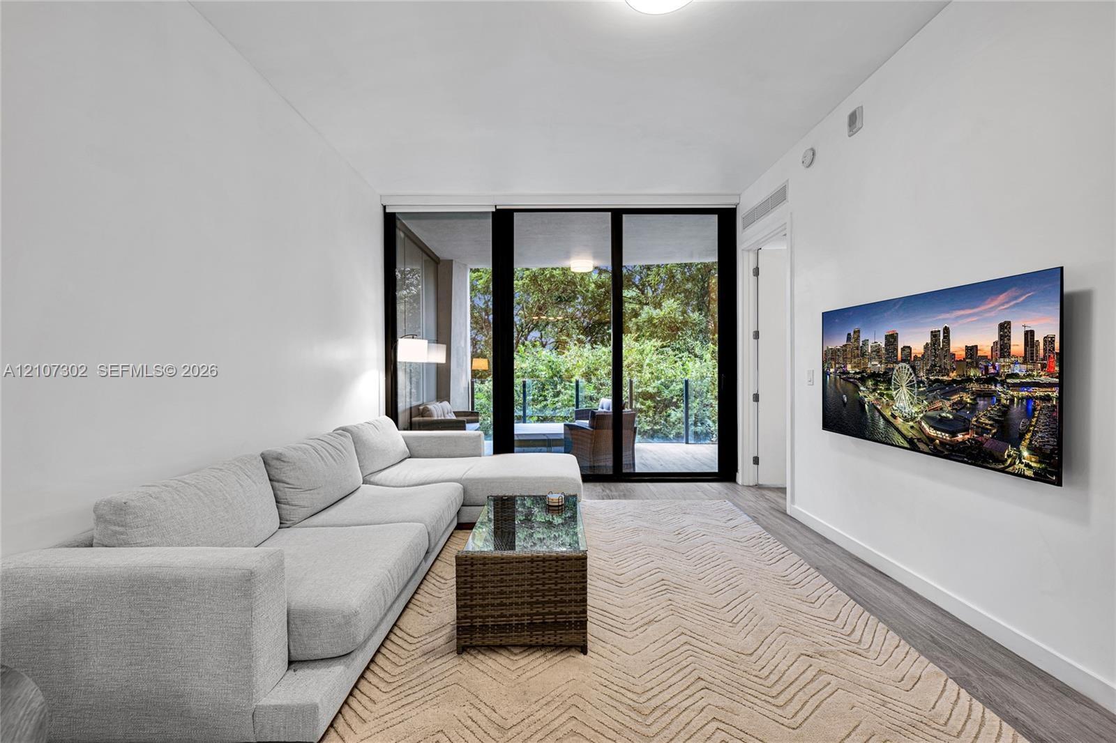 Living area featuring floor-to-ceiling glass sliding doors, wood-finish flooring, and an exterior balcony with glass railing