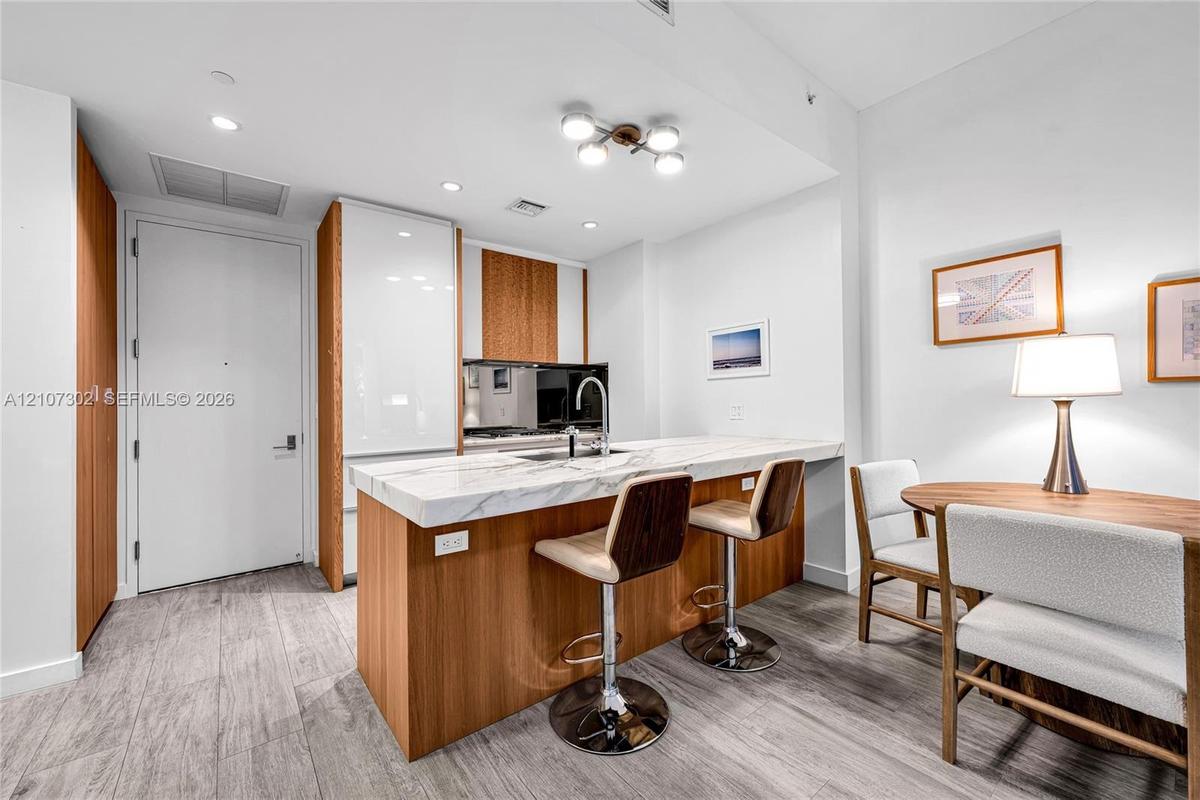 Kitchen featuring wood-finish cabinetry, white high-gloss paneling, integrated refrigerator, stone-composite countertop with waterfall edge, and wood-