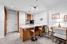 Kitchen featuring wood-finish cabinetry, white high-gloss paneling, integrated refrigerator, stone-composite countertop with waterfall edge, and wood-
