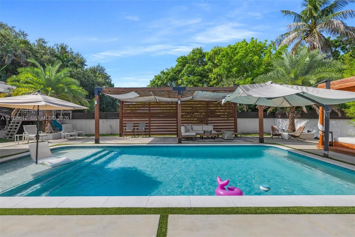 Swimming pool with integrated tanning ledge, paved pool deck, wood-slat pergola, and perimeter fencing