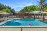 Swimming pool with integrated tanning ledge, paved pool deck, wood-slat pergola, and perimeter fencing
