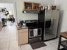 Kitchen area featuring stainless steel side-by-side refrigerator, electric range, stainless steel range hood, natural wood-finish cabinetry, and tiled
