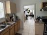 Kitchen featuring light wood-finish cabinetry, laminate countertops, a double-basin stainless steel sink, and ceramic tile flooring