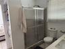 Shower enclosure featuring a chrome-frame sliding door, walk-in design with a tiled threshold, built-in recessed shelving, two-piece toilet, and vanit