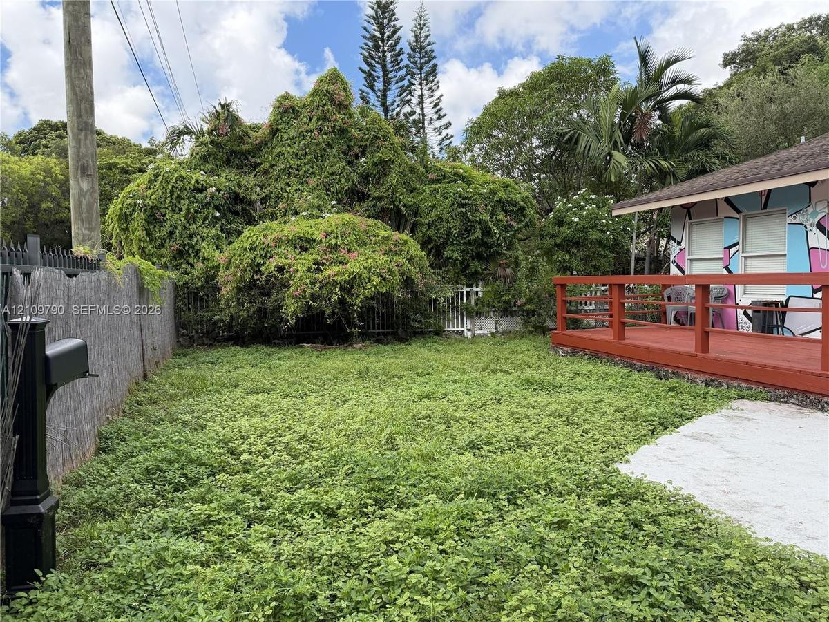 Ground-level wooden deck featuring a perimeter railing, enclosed yard with mature landscaping, and dedicated mailbox post