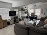 Living area featuring large format neutral tile flooring, neutral wall tones, multiple windows with integrated blinds, a central ceiling fan, and a pr