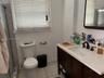 Bathroom featuring a dark wood-finish vanity, light-toned stone countertop, undermount sink with dark metal hardware, ceramic floor tile, and shower e