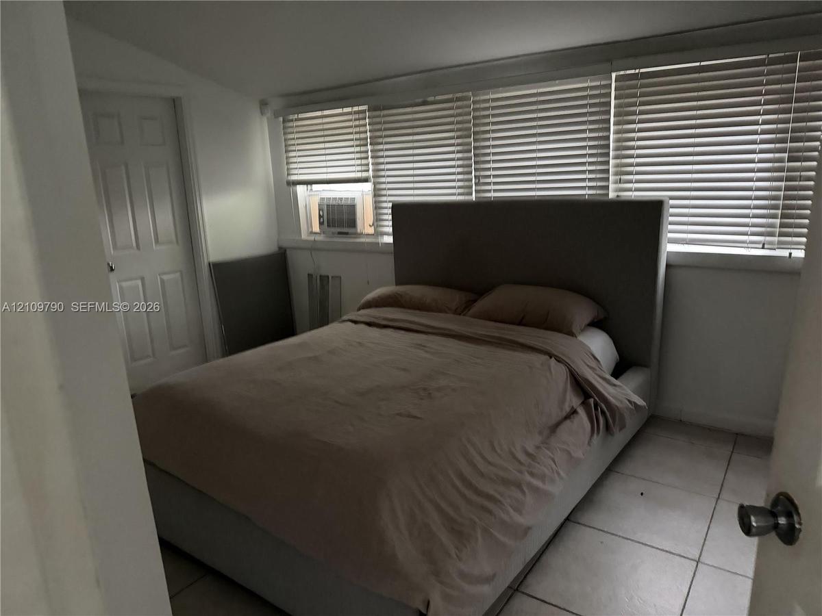 Room featuring neutral tile flooring, a multi-panel door, and a wall of windows fitted with horizontal blinds