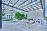 Outdoor terrace featuring an overhead pergola, built-in kitchen station with a stainless steel grill and sink, stone-finish flooring, and manicured la