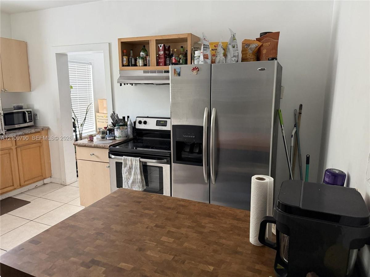 Kitchen featuring light-finish wood cabinetry, stainless steel refrigerator, integrated range, wood-block countertop island, and tile flooring