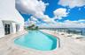 Rooftop pool featuring light-toned stone tile decking, a glass panel perimeter railing, and concrete structural elements