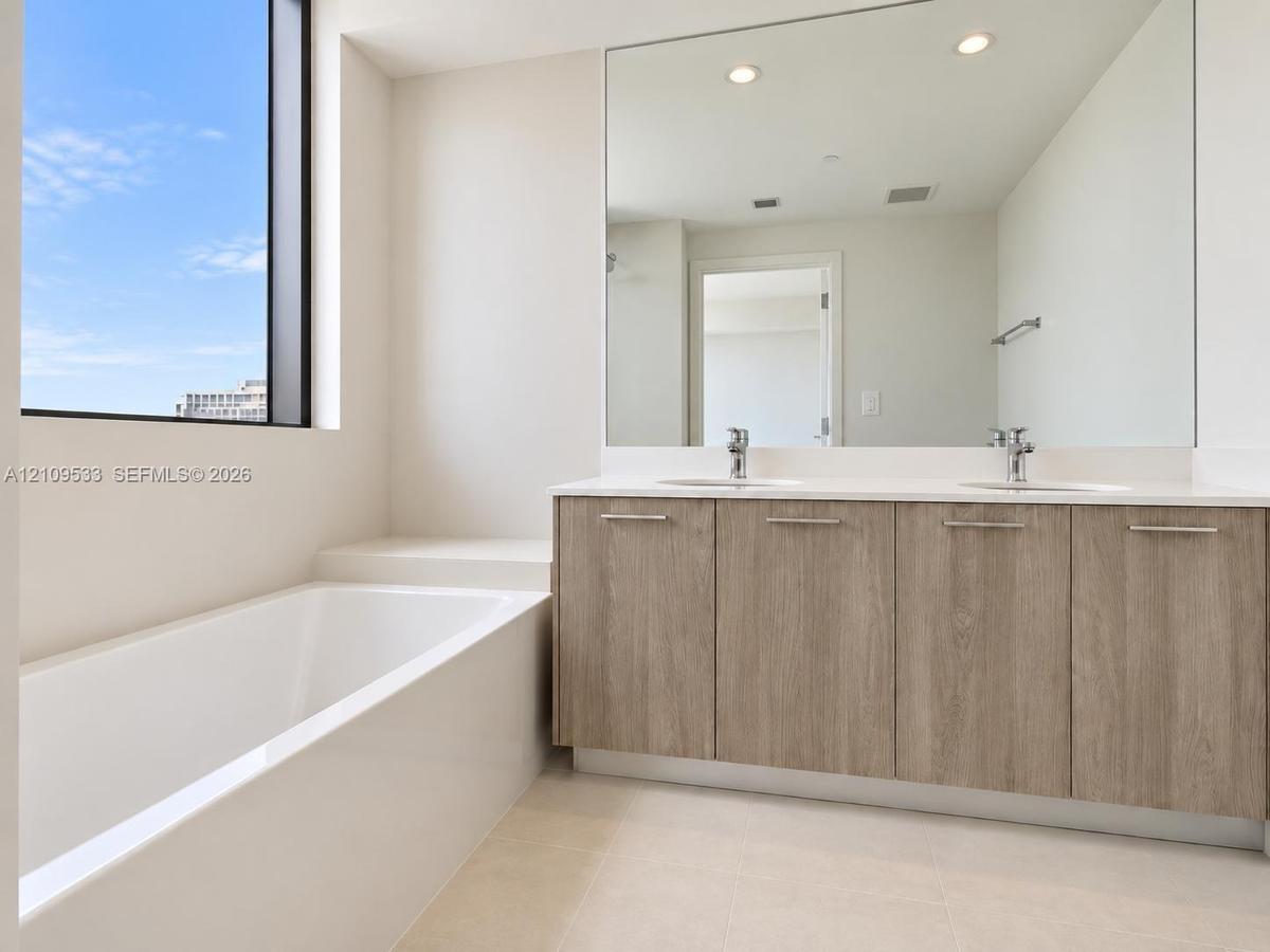 Bathroom featuring a double-sink vanity with wood-finish cabinetry, a white countertop, an integrated soaking tub, and a floor-to-ceiling window