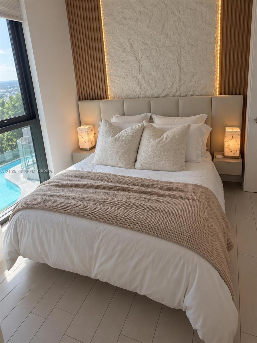 Floor-to-ceiling windows, vertical wood-slat wall paneling, integrated stone accent wall, light-toned tile flooring, and wall-mounted bedside cabinetr