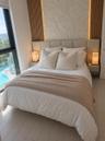 Floor-to-ceiling windows, vertical wood-slat wall paneling, integrated stone accent wall, light-toned tile flooring, and wall-mounted bedside cabinetr