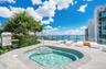 Rooftop terrace featuring an in-ground spa, stone tile decking, glass perimeter railing, and mature palm landscaping