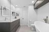 Modern dual vanity with stone countertop, freestanding soaking tub, wall-mounted faucets, and dark wood-finish cabinetry