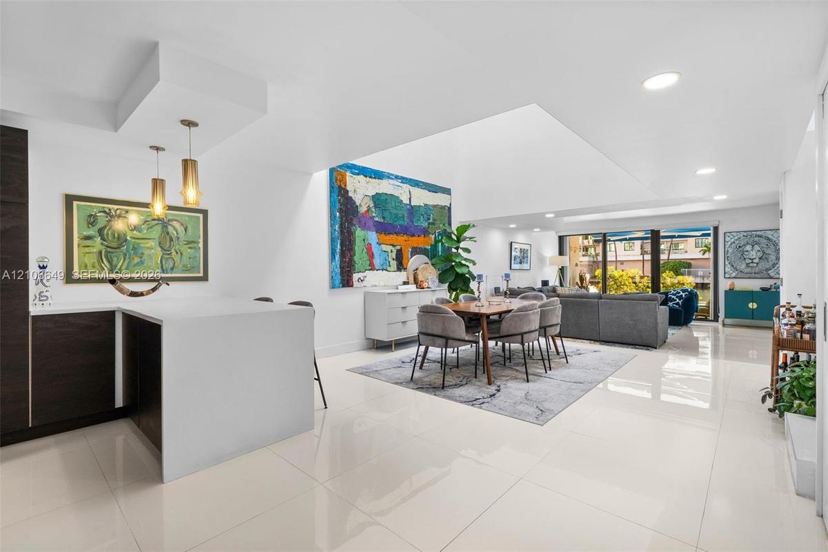 Open-concept living space featuring white polished tile flooring, recessed ceiling lighting, a waterfall-edge kitchen island, dual pendant lights, and