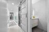 Sliding door entry concealing stacked laundry appliances, textured geometric wall tiling, modern wall-mounted vanity, and glass panel railing