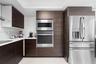 Modern kitchen featuring dark wood-finish cabinetry, solid surface countertops, stainless steel wall oven, built-in microwave, and stainless steel fre