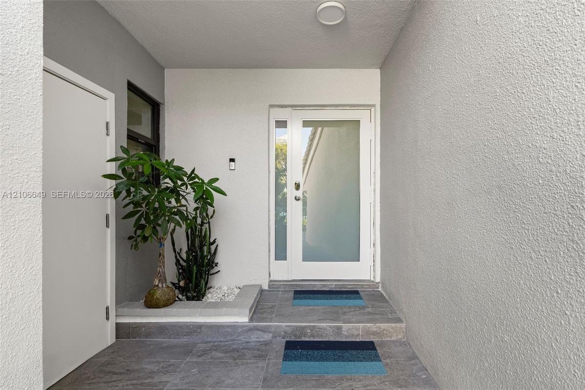 Entryway featuring a white door with a frosted glass panel, recessed ceiling lighting, textured wall finish, grey tiled flooring, and a built-in stone