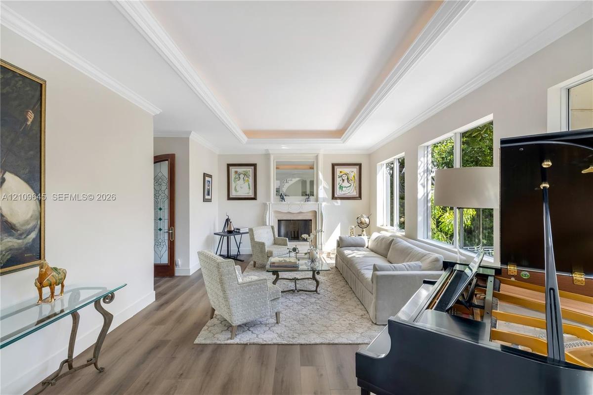 Living area featuring a tray ceiling, wood-finish flooring, a traditional fireplace with a decorative mantel, and multi-pane windows