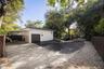 Detached garage with a multi-vehicle driveway, covered carport, mature tree canopy, and wood-slat perimeter fencing