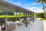 Covered patio featuring a structured metal pergola, large-format stone pavers, and a perimeter of mature privacy hedging