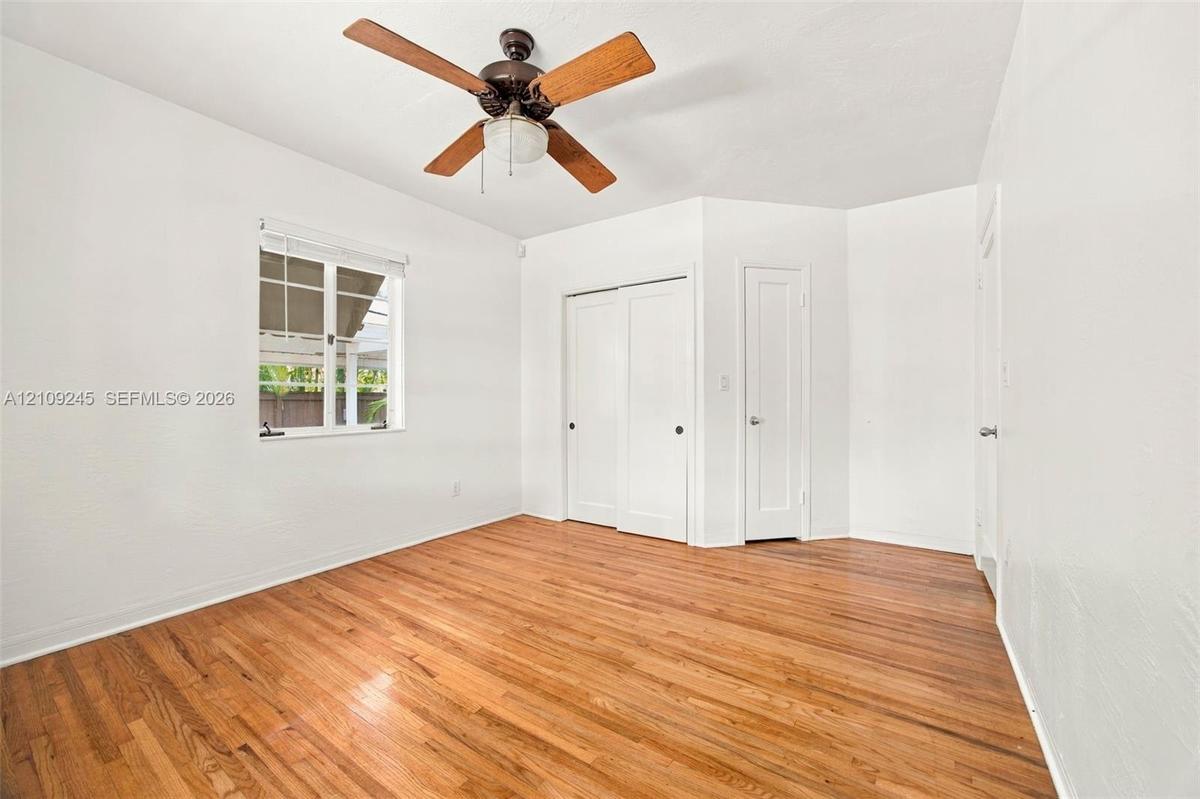 Interior room featuring wood-finish flooring, a multi-blade ceiling fan with central lighting, dual sliding closet doors, and a single-panel interior 