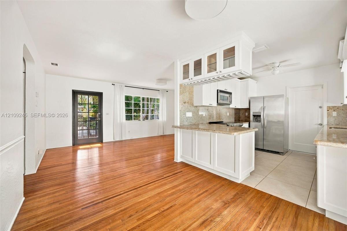 Kitchen featuring white shaker-style cabinetry, stone countertops, stainless steel appliances, wood-finish flooring, and a glass-paneled exterior door