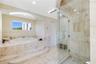 Jetted soaking tub with a stepped stone surround, walk-in shower with glass enclosure, stone tile flooring, and recessed ceiling lighting