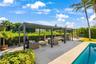 Outdoor living space featuring a modern metal pergola, paved stone pool deck, and inground swimming pool surrounded by mature landscape hedging