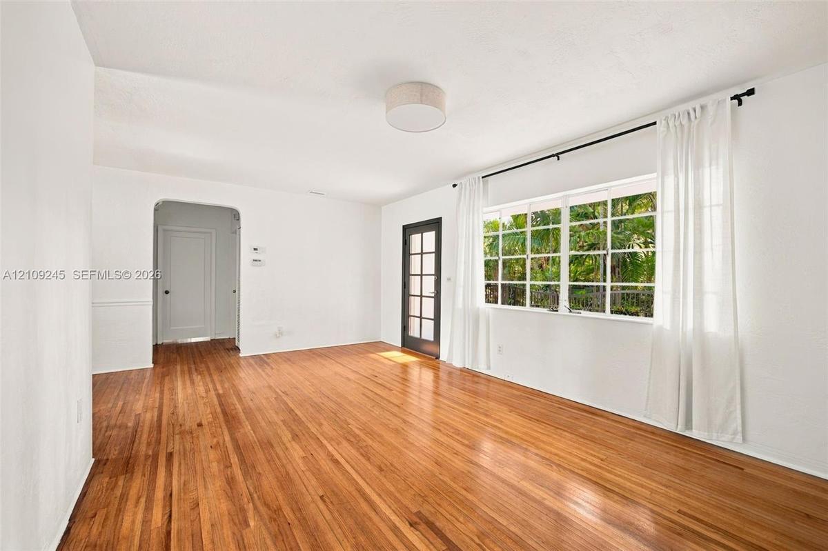 Living space featuring polished wood-finish flooring, a large multi-pane window, an arched doorway, and a glass-paneled exterior door