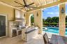 Covered outdoor kitchen featuring stone countertops, a stainless steel grill, a tile backsplash, and a built-in sink, accented by an arched opening an