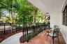 Covered patio featuring terracotta-style tile flooring, black metal railing, and a concrete walkway bordered by mature landscaping and tall palms