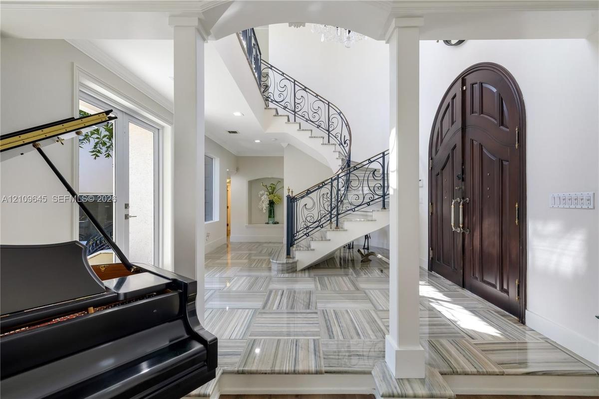 Foyer featuring arched double entry doors, curved staircase with ornamental metal railings, stone flooring with linear patterns, recessed lighting, an