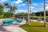 Backyard featuring an in-ground swimming pool, attached spa, stone-finish pool deck, synthetic turf lawn, and metal-frame pergola