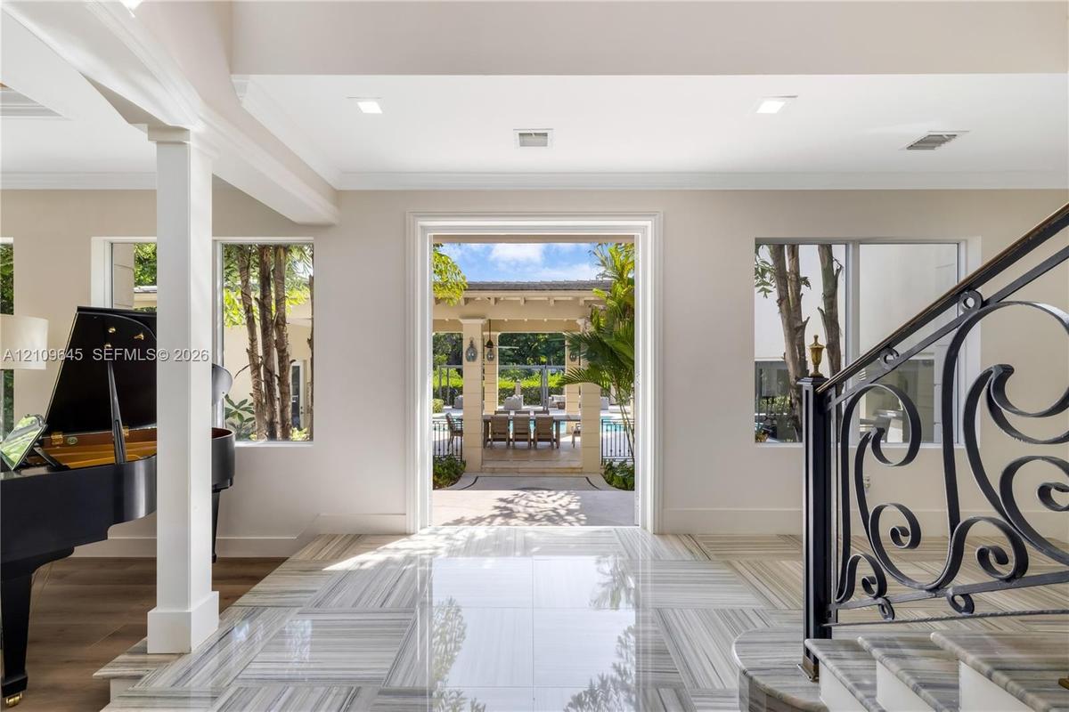 Foyer featuring large-format light-toned stone flooring, decorative iron stair railing, recessed ceiling lighting, and expansive square-cased entry to